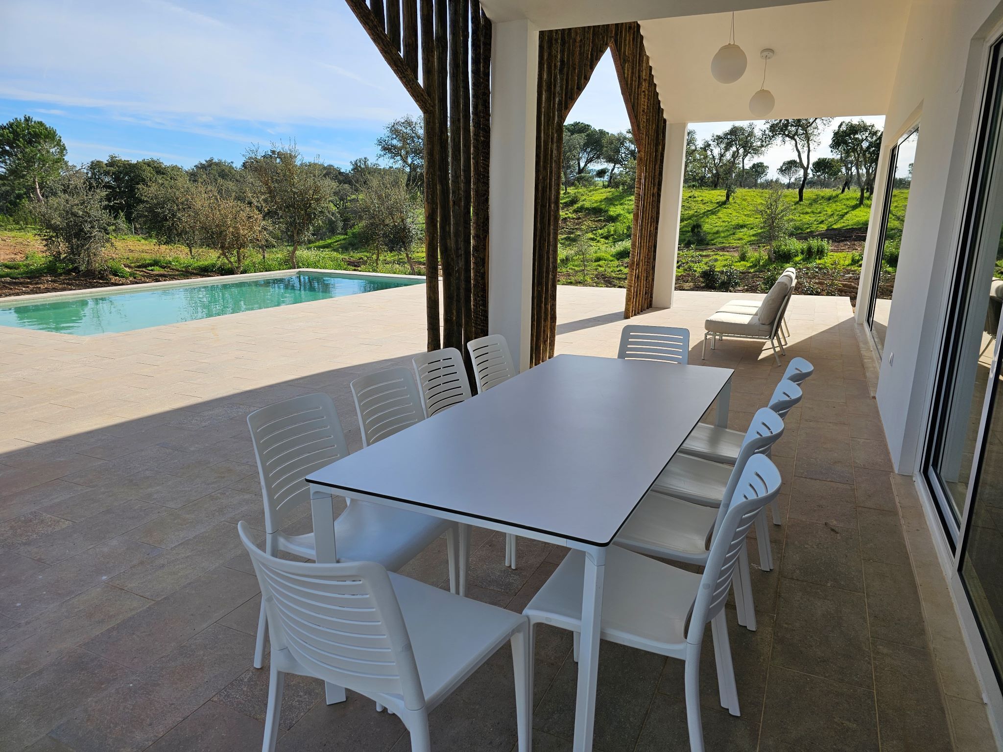 A covered patio with a pool, white plastic chairs, and a table.