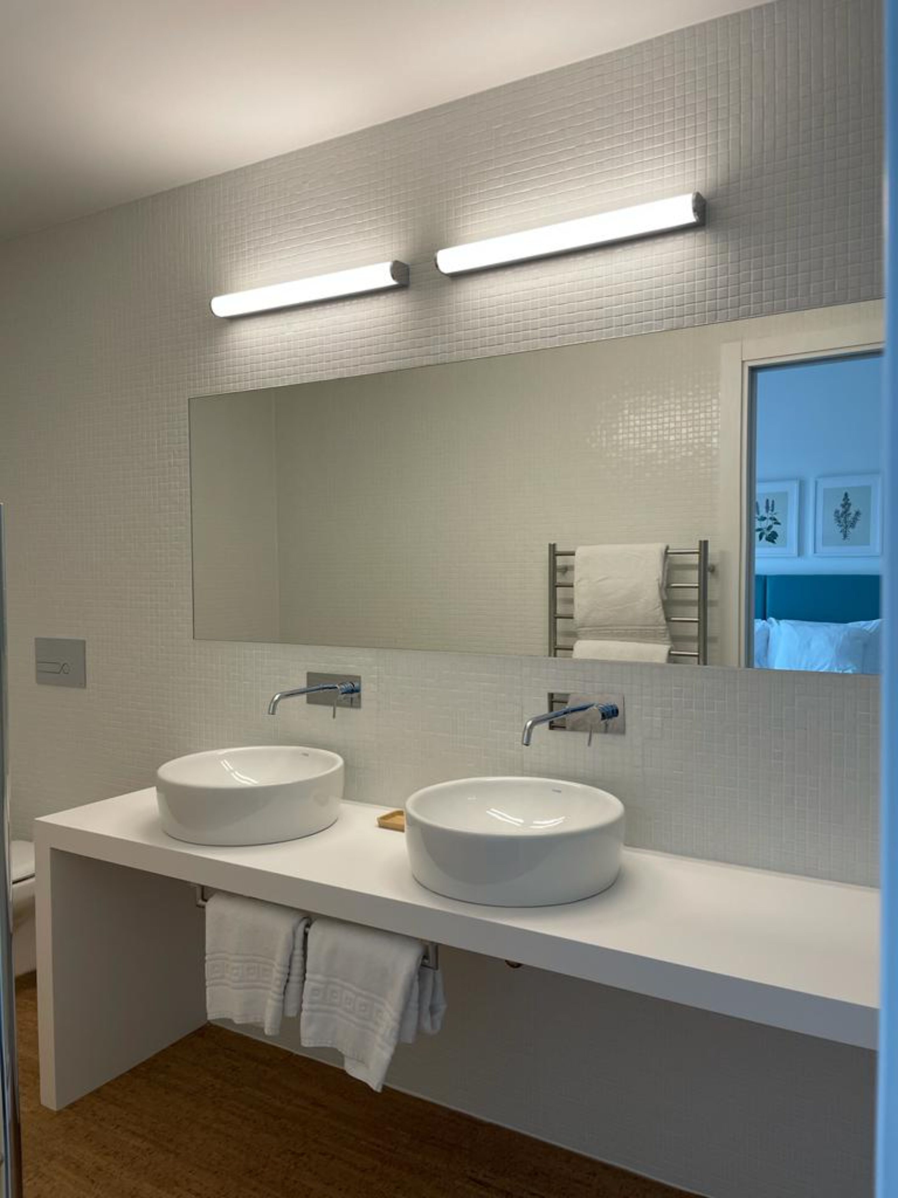 Un baño moderno con dos lavamanos blancos, un espejo grande e iluminación en el techo.