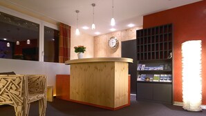 A reception area with a wooden reception desk, a clock, and a bookshelf with brochures. - Hotel Hohe Promenade Arosa (Arosa)