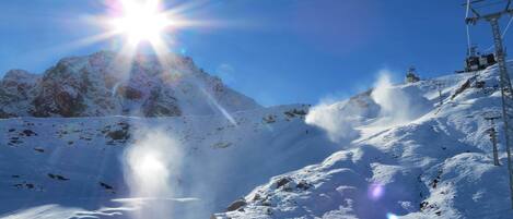A snowy mountain landscape with a clear sky and a bright sun.