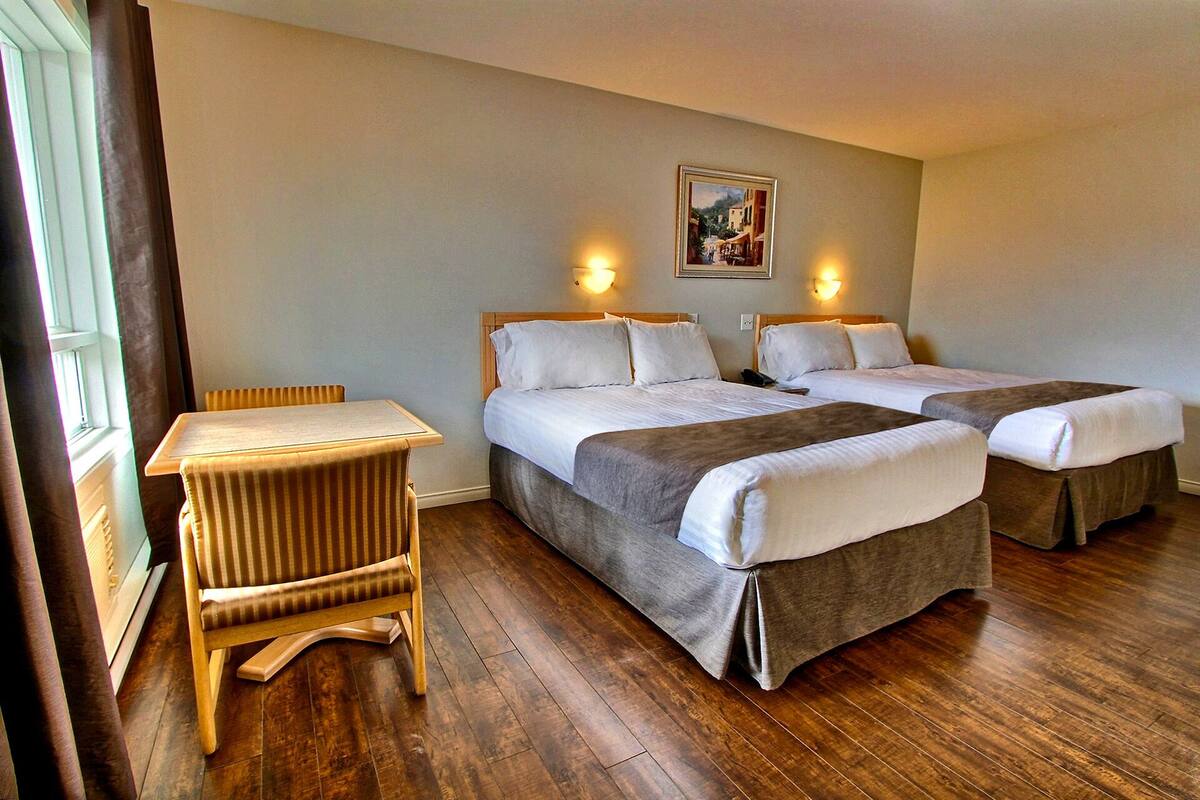 A hotel room with two beds, a wooden chair, and a table.