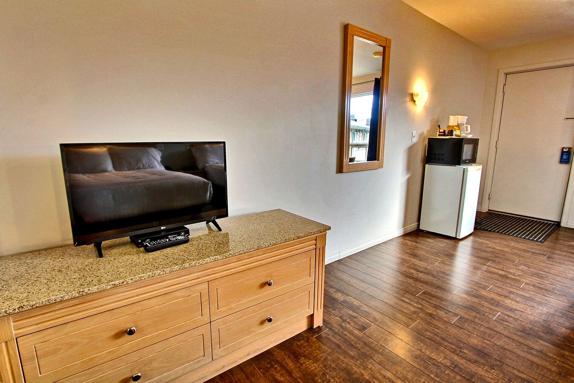 A hotel room with a wooden dresser, a television, a microwave, and a refrigerator.