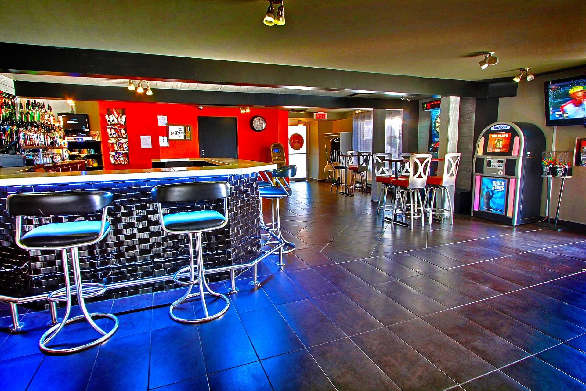 Una zona de bar con taburetes, una barra y una pantalla de televisión.