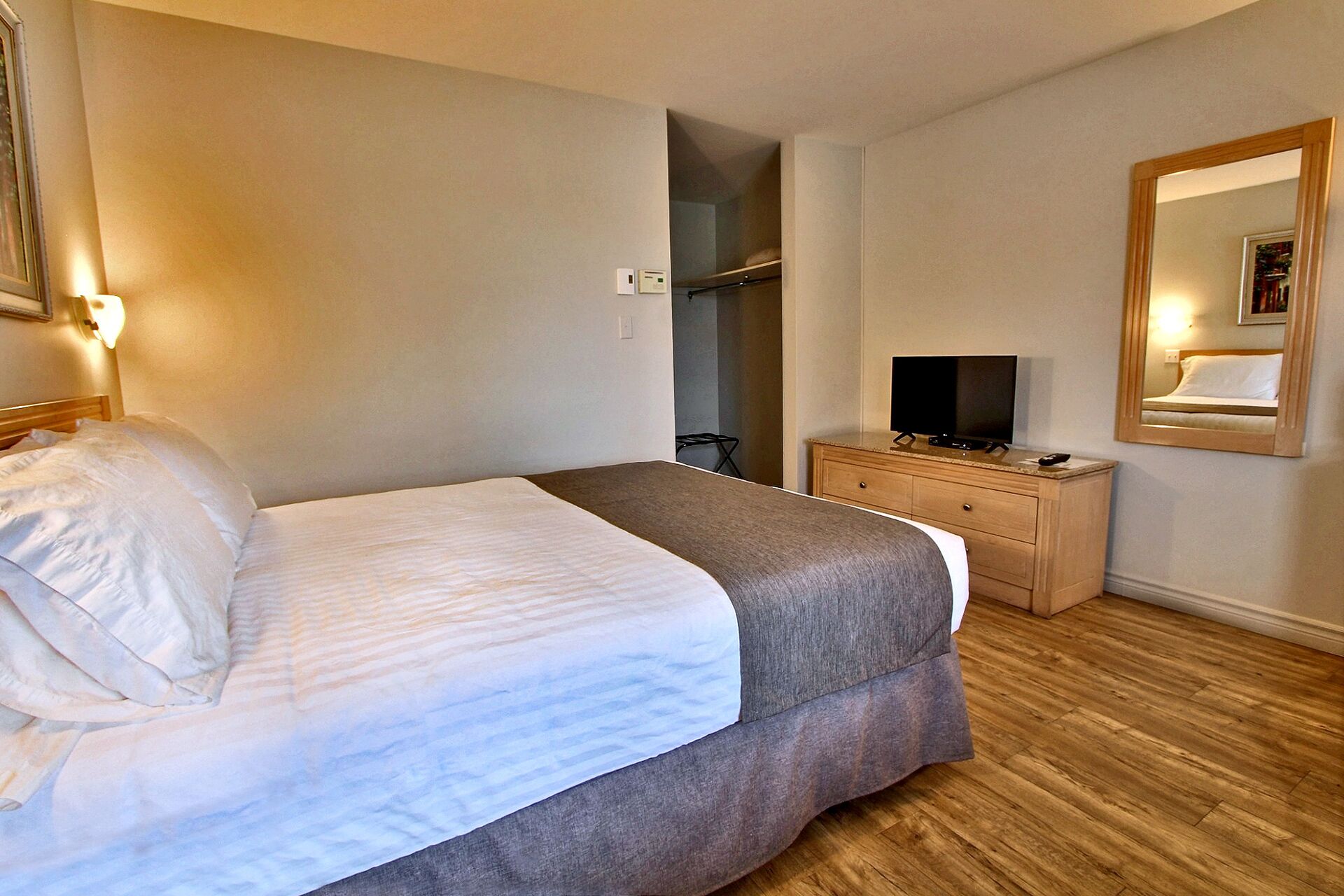 Una habitación de hotel con cama, televisor en un aparador de madera, espejo y armario.