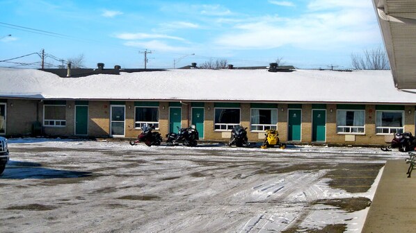 Un motel con varias habitaciones, un estacionamiento y nieve en el suelo.