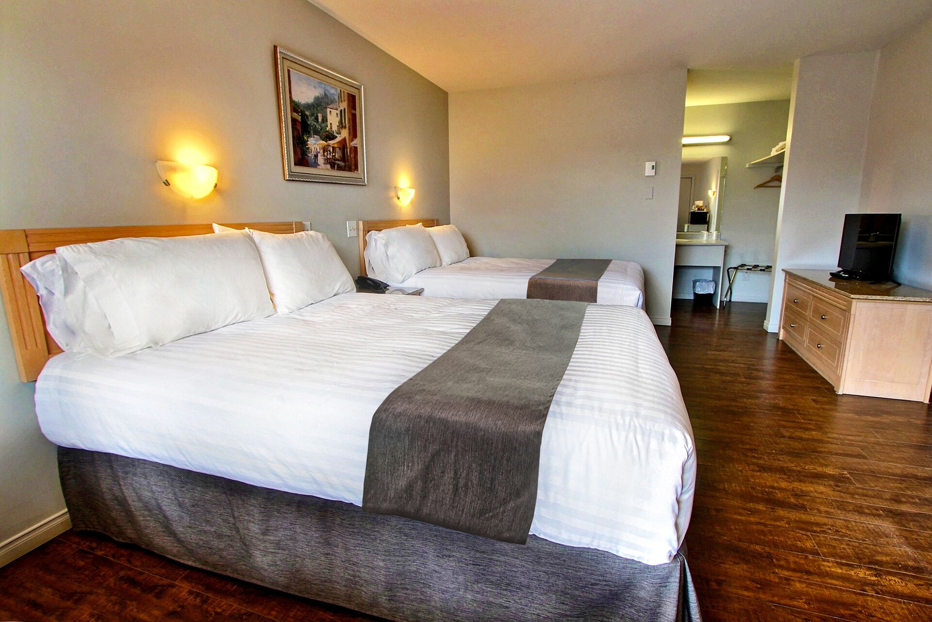 Een hotelkamer met twee bedden, een bureau, een televisie en een schilderij aan de muur.