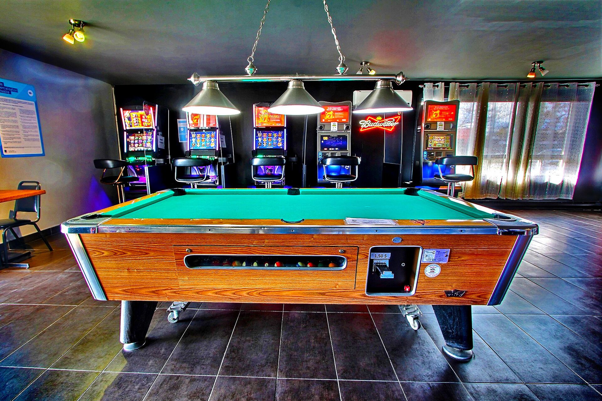 A pool table with a wooden finish, overhead lighting, and a neon sign in the background.