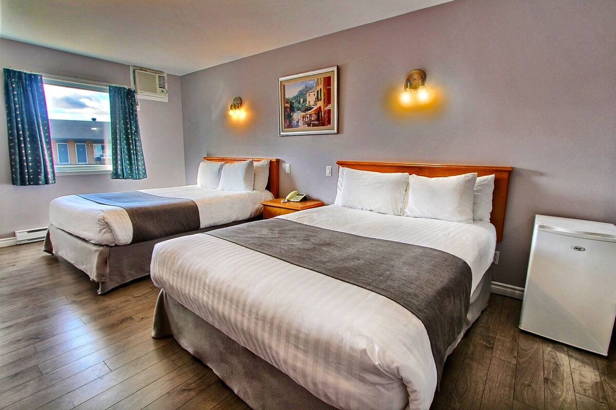 A hotel room with two beds, a small desk, a refrigerator, and a painting on the wall.
