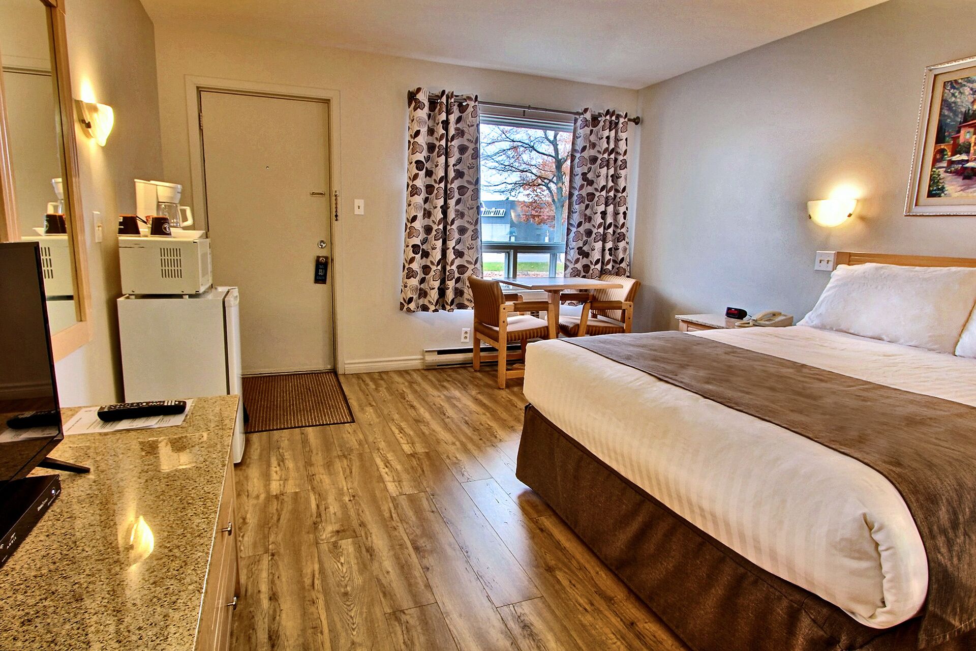 Ein Hotelzimmer mit einem Bett, einem Schreibtisch, einem Stuhl, einem Kühlschrank, einer Mikrowelle und einem fenster mit Vorhängen.