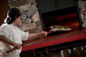 Een kok gebruikt een houten spatel om een pizza uit een oven met stenen te halen.