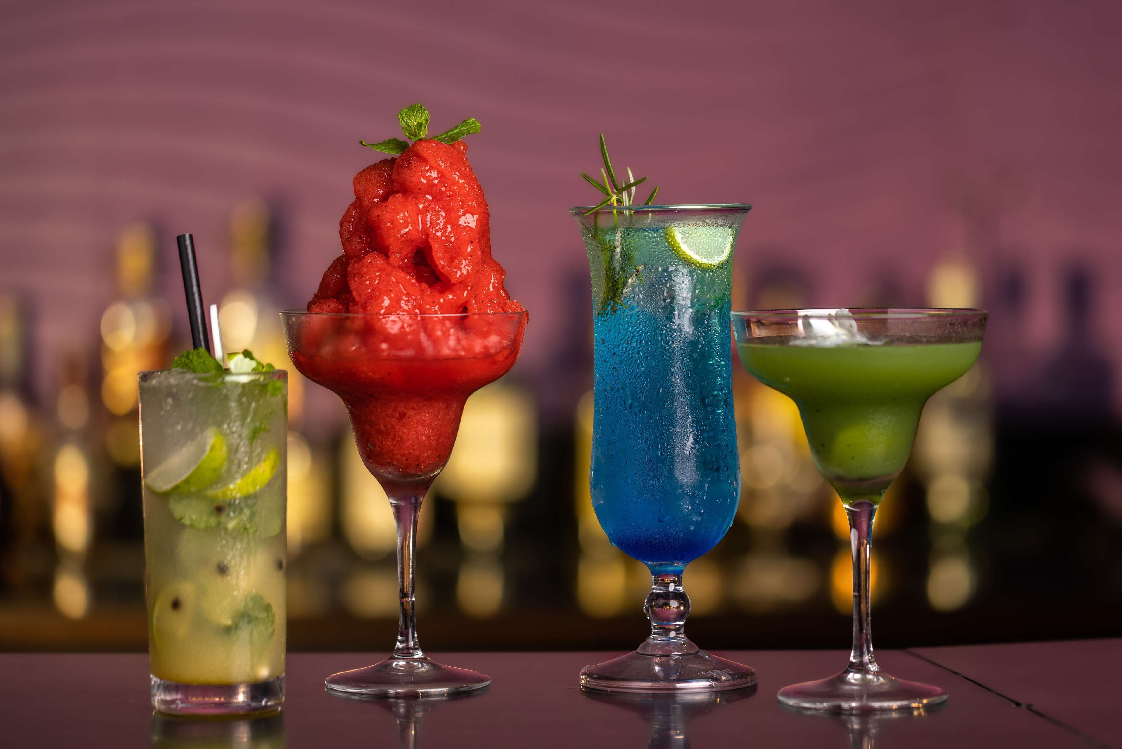 Three cocktails with different colors and garnishes on a bar counter.