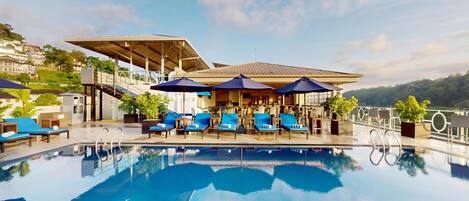 A pool area with lounge chairs and umbrellas, a covered seating area, and a view of the surrounding landscape.