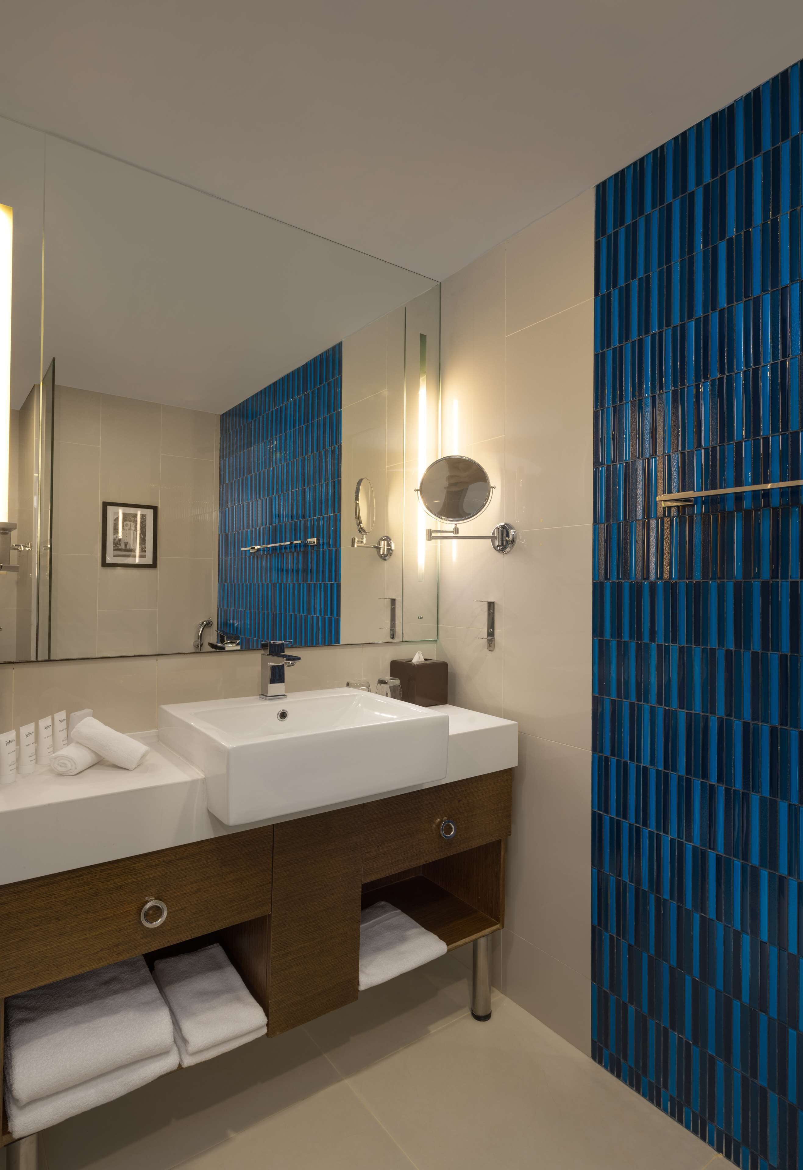 Un baño moderno con lavamanos doble, un espejo grande y paredes de azulejos azules.