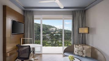 A modern room with a balcony, a TV mounted on the wall, a dining table with chairs, and a sofa with cushions.