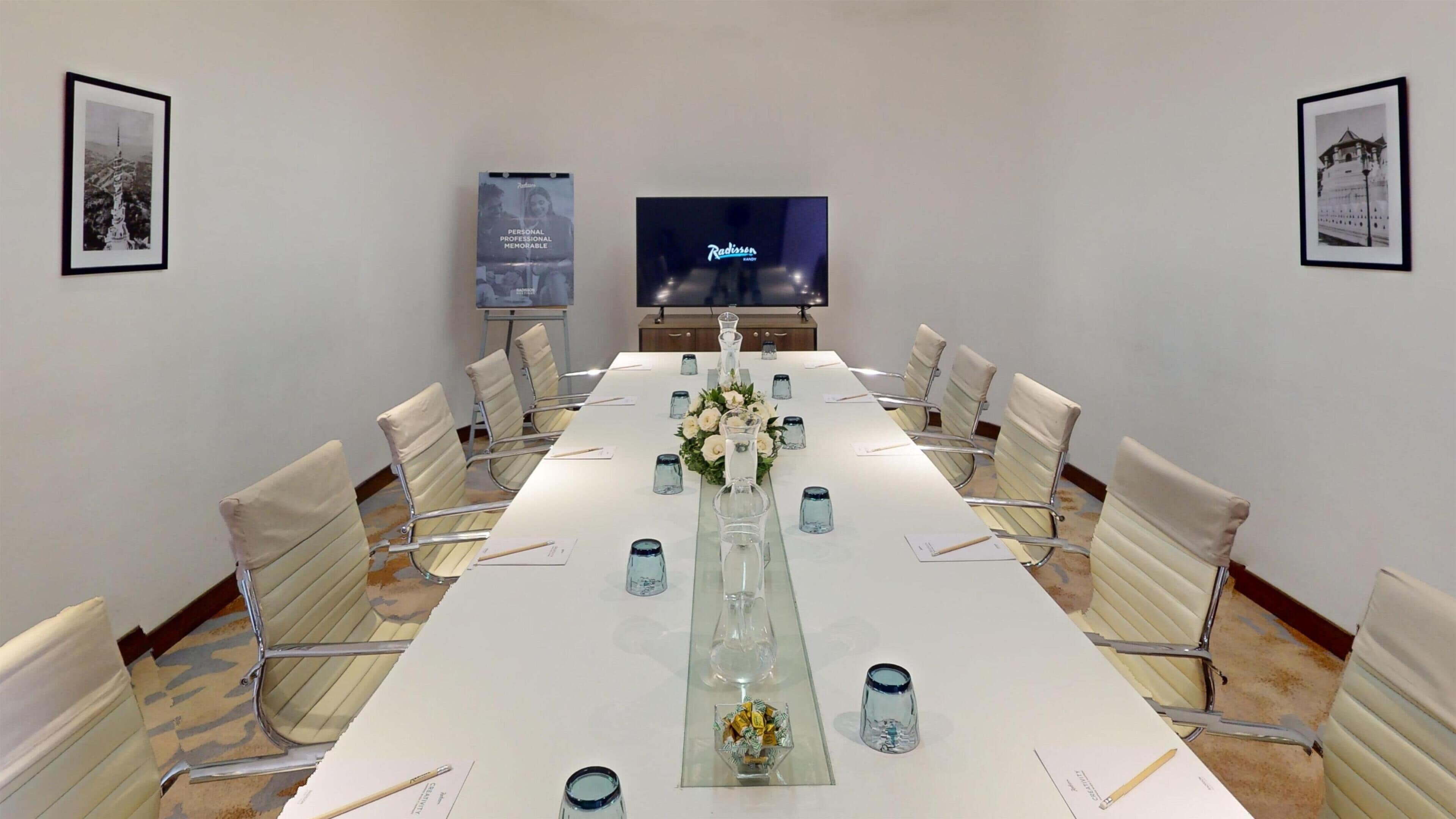 Un salón de conferencias con una larga mesa, sillas, una pantalla de televisión y cuadros en las paredes.