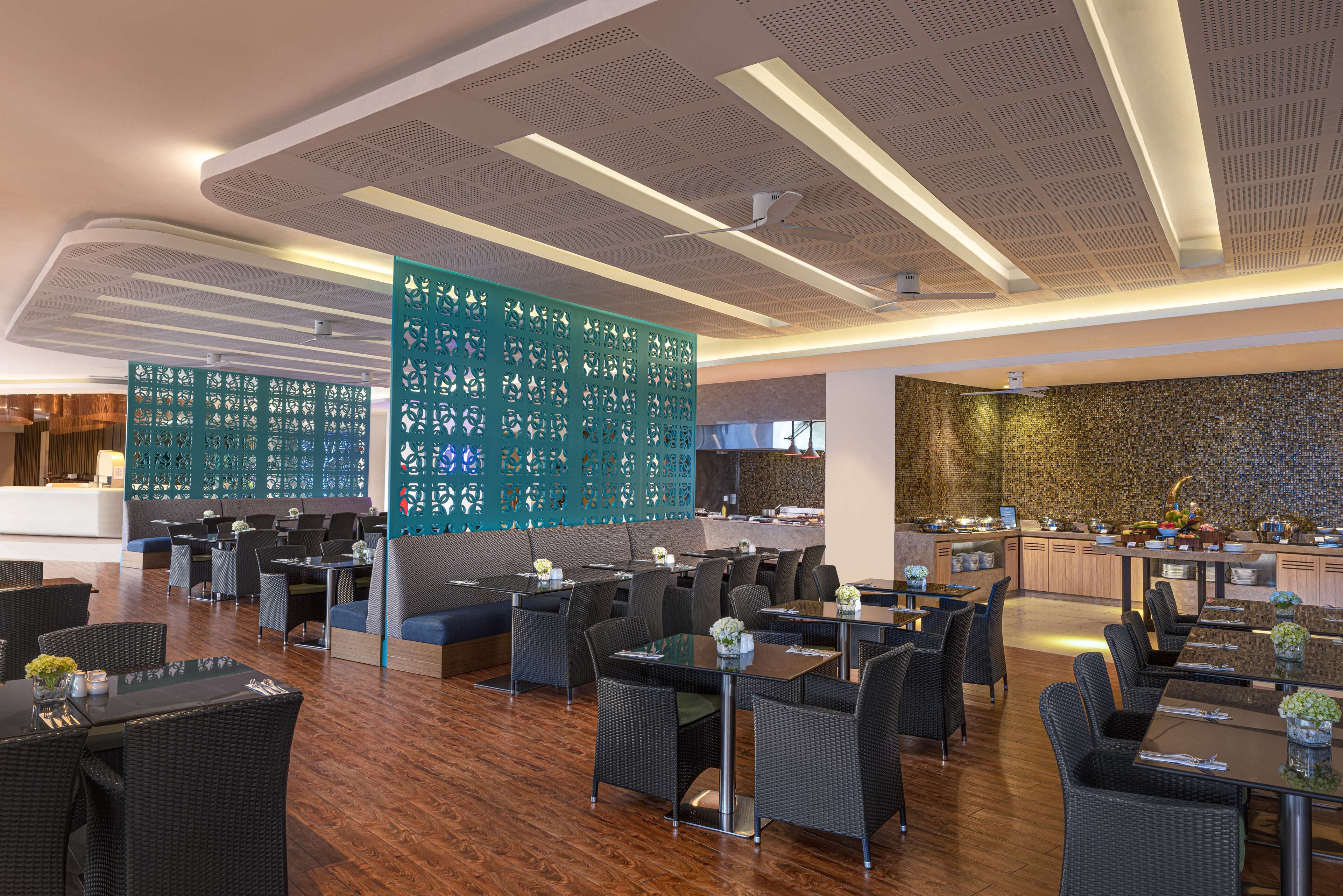 Un restaurante moderno con techos altos, una pared con diseño y diversas opciones de asientos, incluyendo mesas y cabinas.