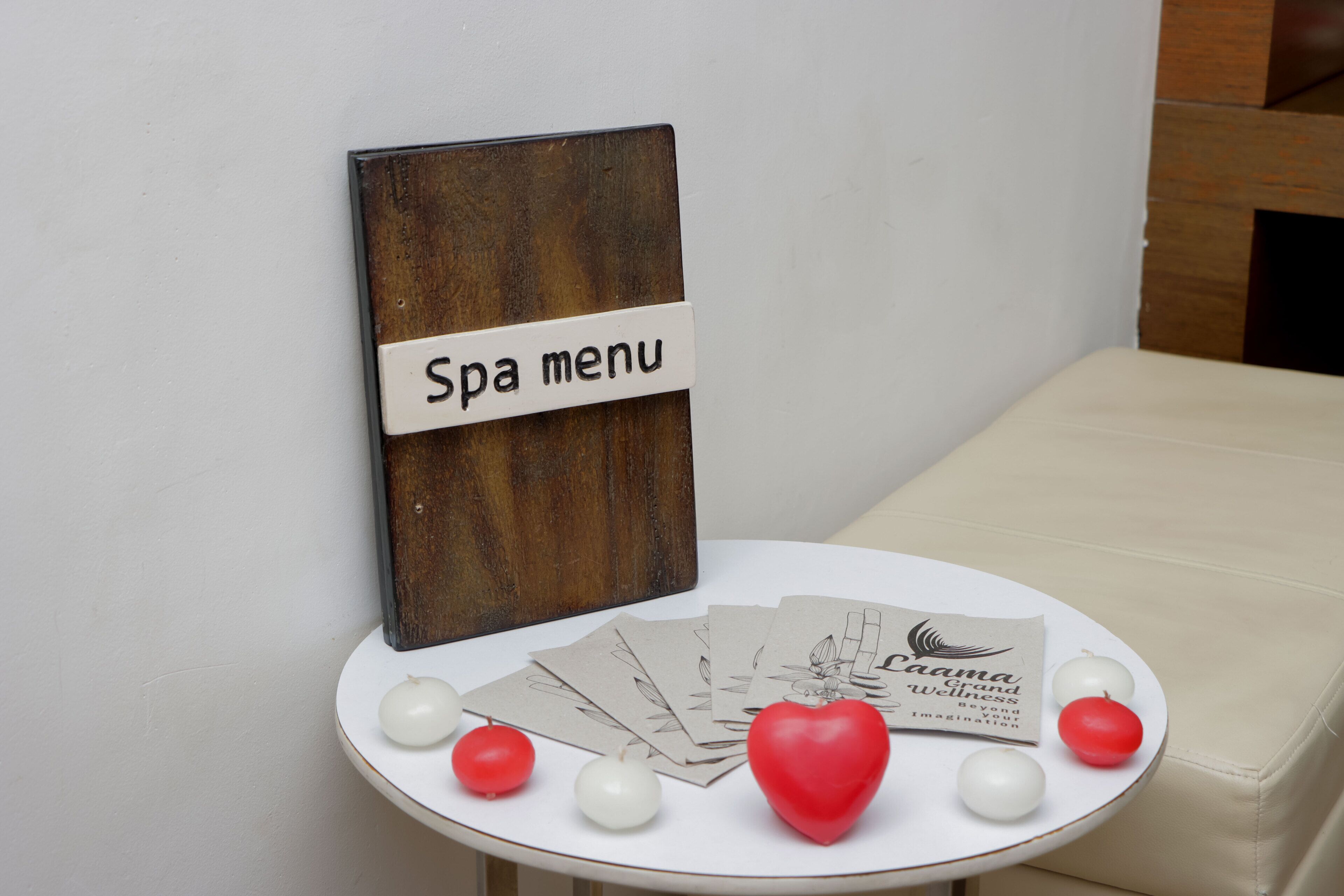 Un cartel de menú de spa sobre un tablero de madera, una mesa blanca con borde redondeado, varias tarjetas de spa y bolas decorativas.