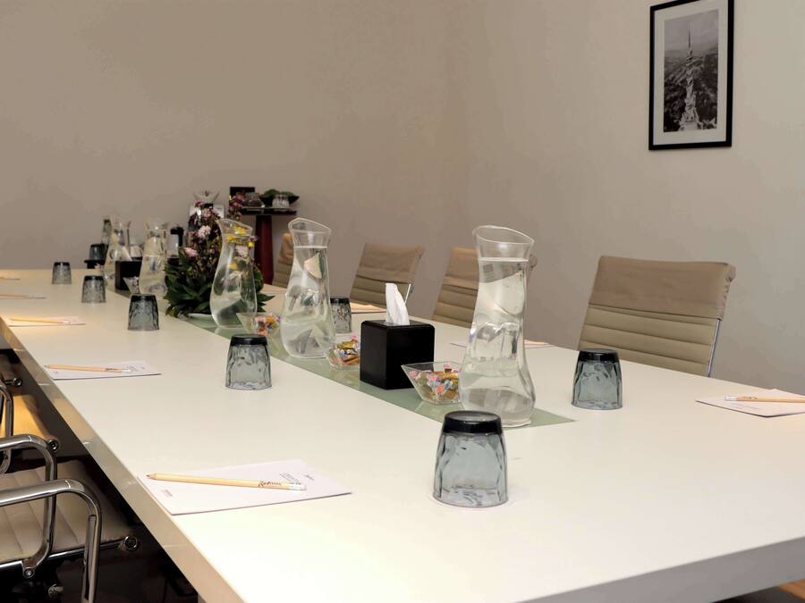 A conference room with a long table, chairs, and various items like glass pitchers, a tissue box, and a framed picture on the wall.