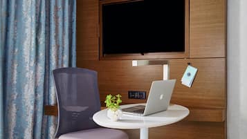 A modern room with a TV mounted on the wall, a laptop on a small table, a chair, and a plant.