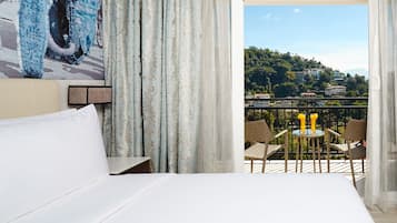 Habitación de hotel con balcón, cama y vistas a un paisaje urbano.