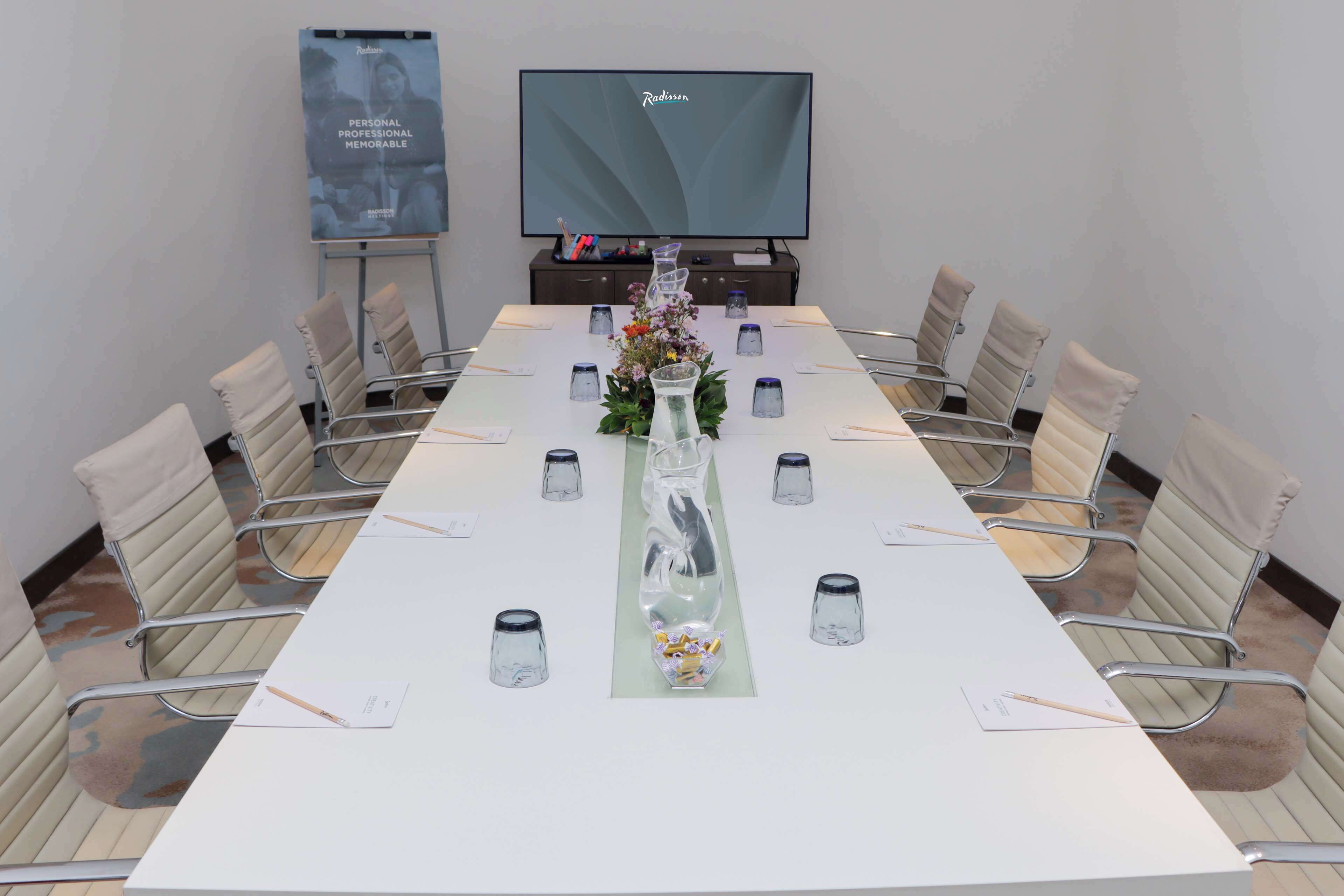 A conference room with a long table, chairs, a television, and a poster on the wall.