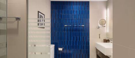A modern bathroom with a white toilet, a blue-tiled shower wall, and a wooden vanity with a mirror.