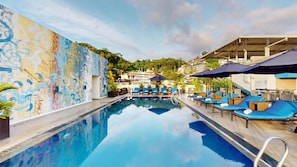 A swimming pool with lounge chairs and umbrellas, surrounded by a colorful mural and greenery. - Radisson Hotel Kandy (Kandy)