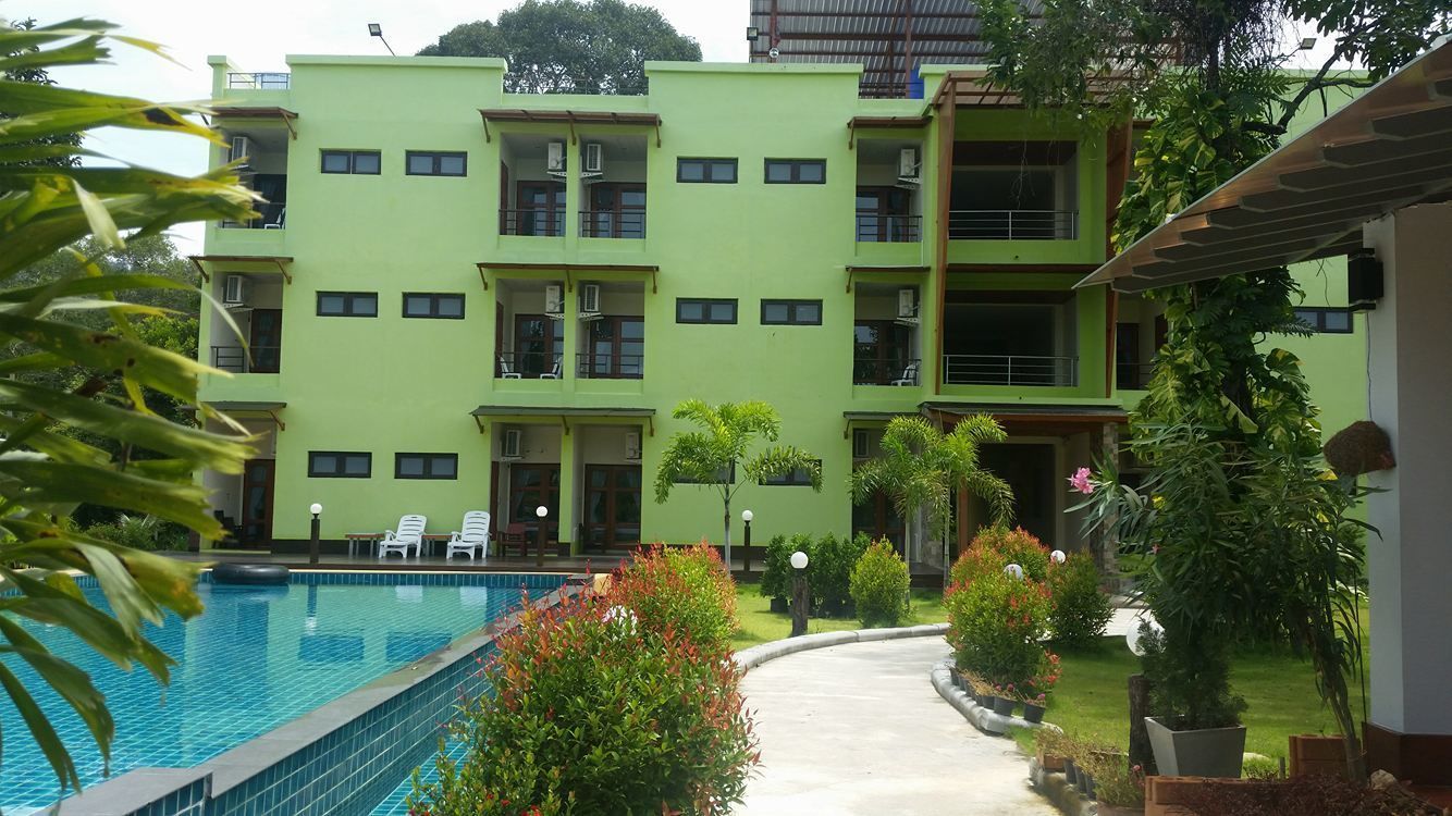 A multi-story building with a swimming pool, surrounded by greenery and outdoor seating.