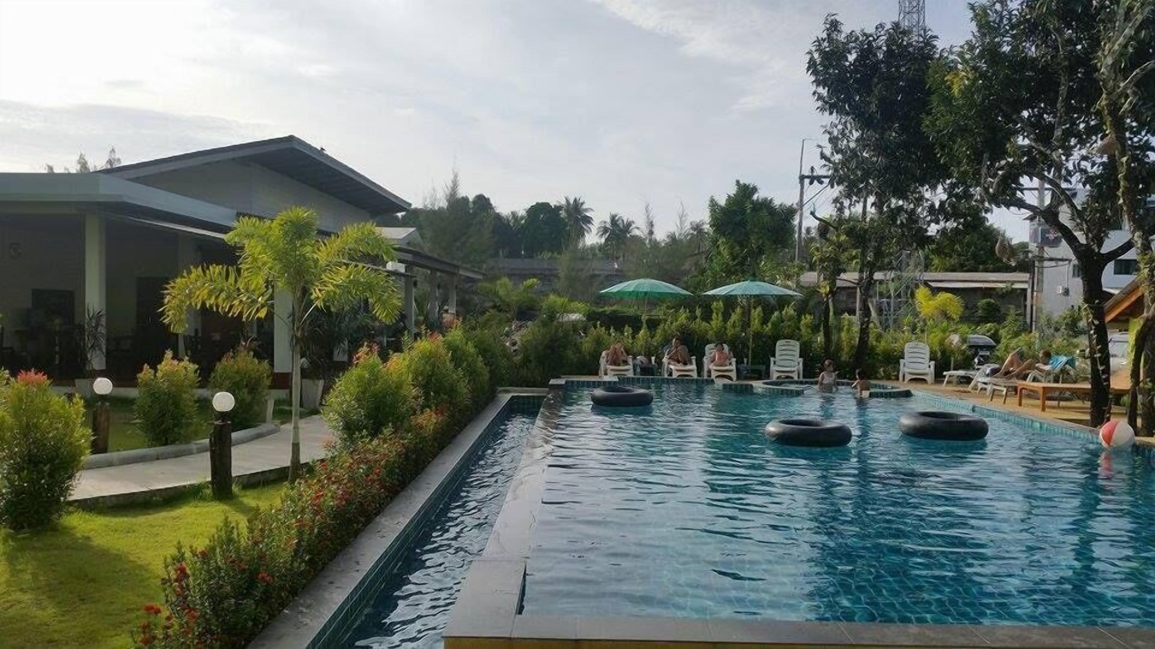 Una piscina con flotadores, rodeada de follaje y sillas de descanso.