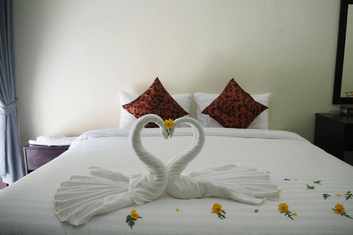 A neatly made bed with a swan-shaped towel arrangement and decorative pillows.