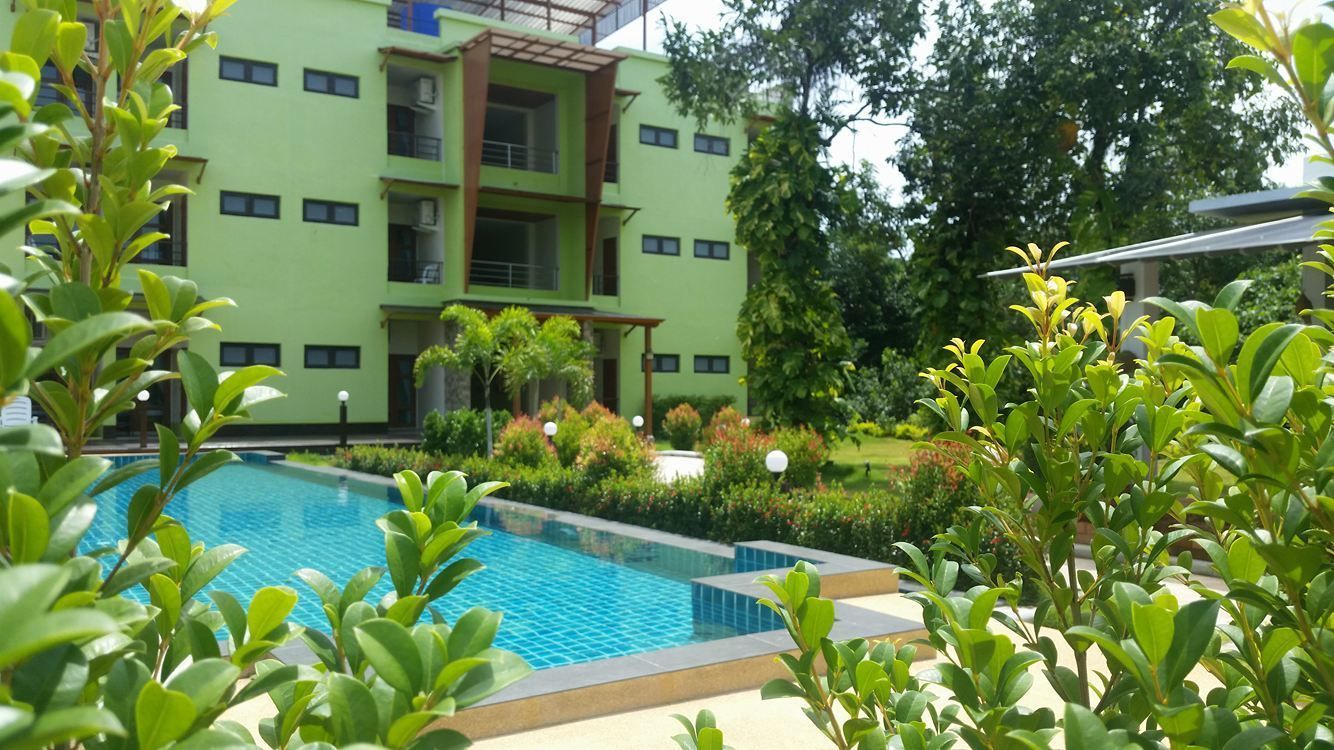 Una piscina rodeada de abundante vegetación y un edificio de varios pisos con balcones.