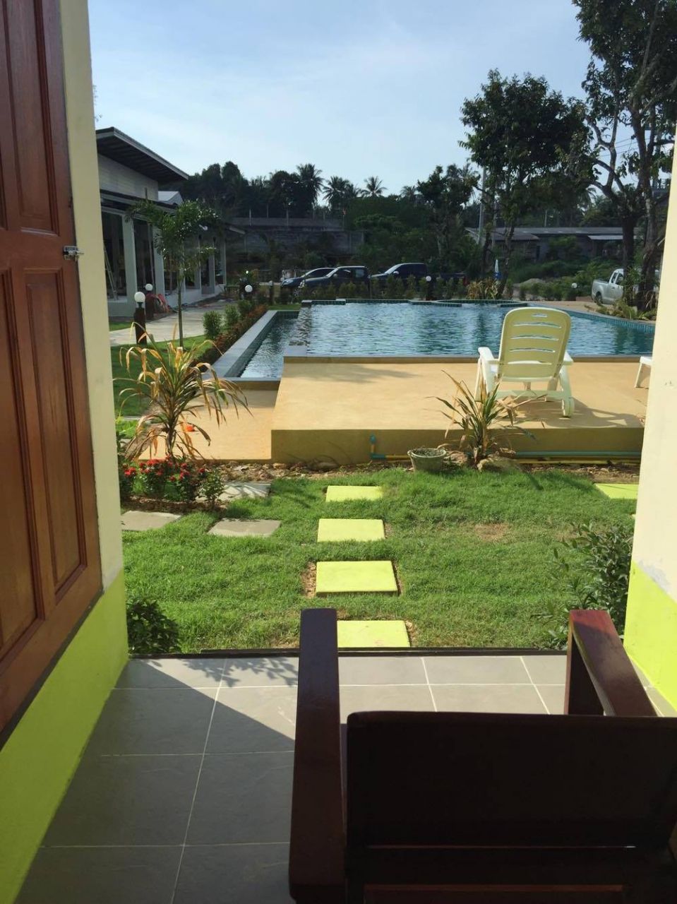 Vista desde un balcón con vista a una piscina, con una silla y un pequeño jardín.