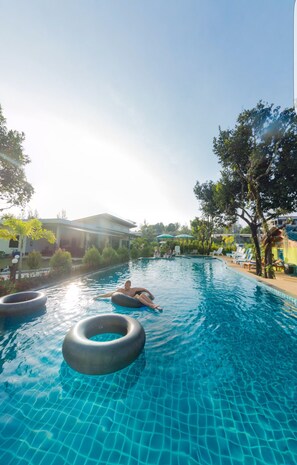 Una piscina con agua azul cristalina, rodeada de árboles y sillas de descanso.