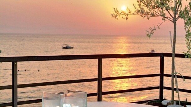 A table with a glass of water and a menu, overlooking a sunset over the sea.