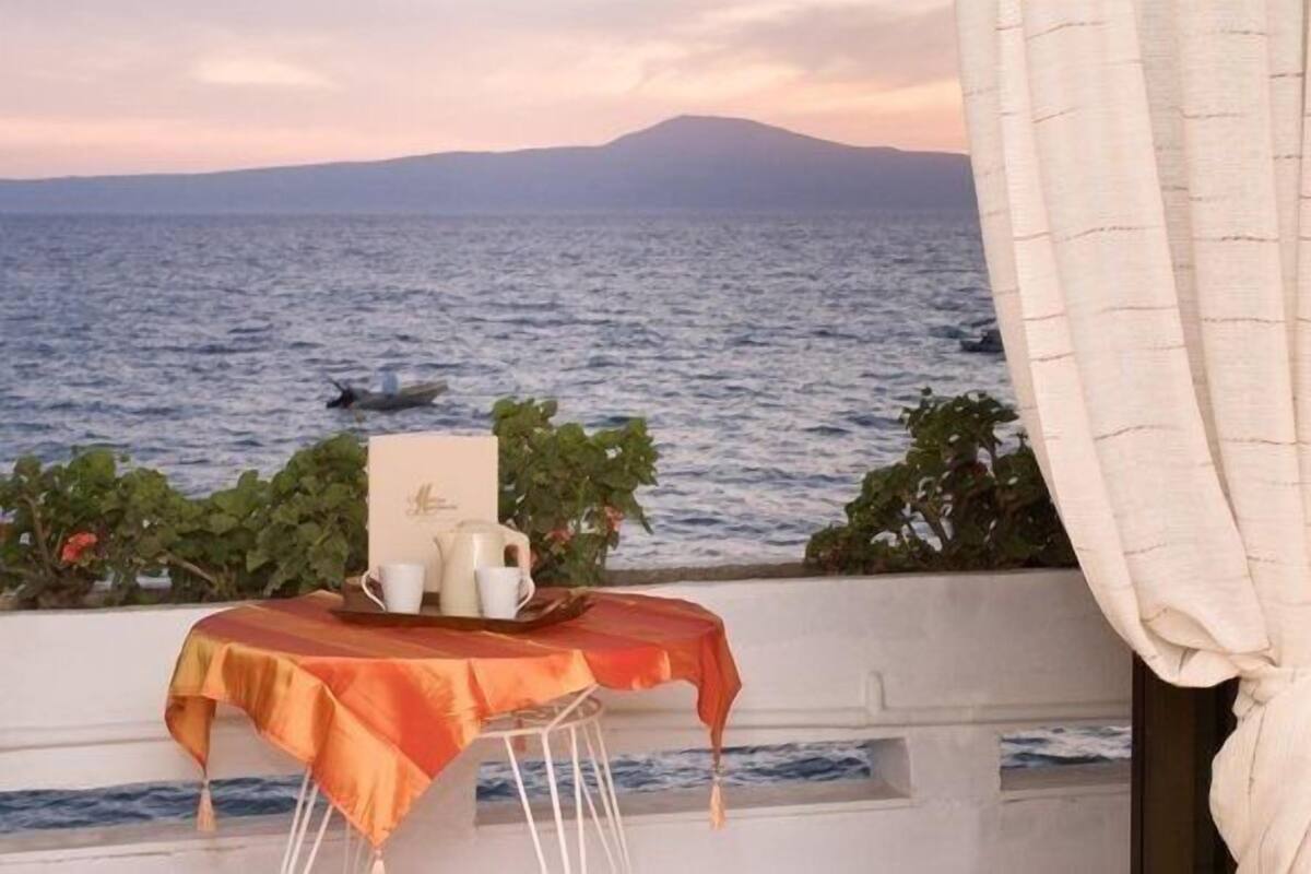 A table with a tablecloth and a tray set up on a balcony overlooking the sea with a mountain in the background.