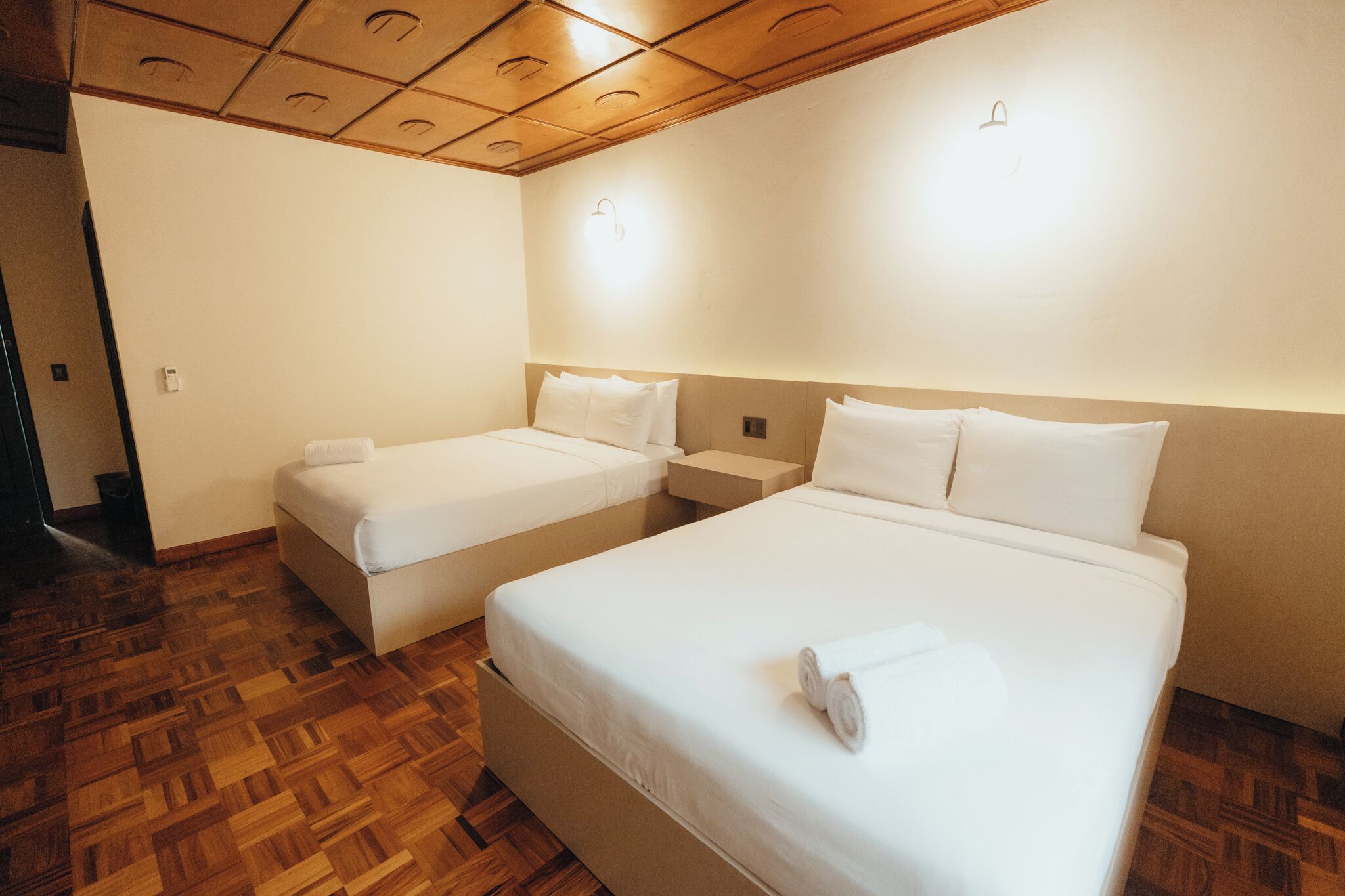 Una habitación de hotel con dos camas individuales, suelo de madera y techo de madera.