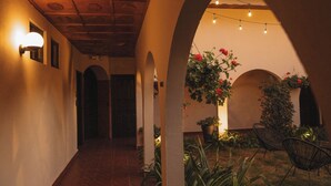 Un pasillo con arcos, una planta en maceta con flores y guirnaldas luminosas.