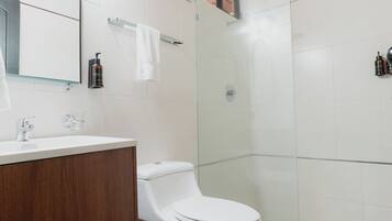 A modern bathroom with a wooden ceiling, white tiles, a white toilet, a wooden vanity, and a glass shower enclosure.