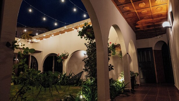 Un patio exterior con arcos, luces colgantes y plantas en macetas.