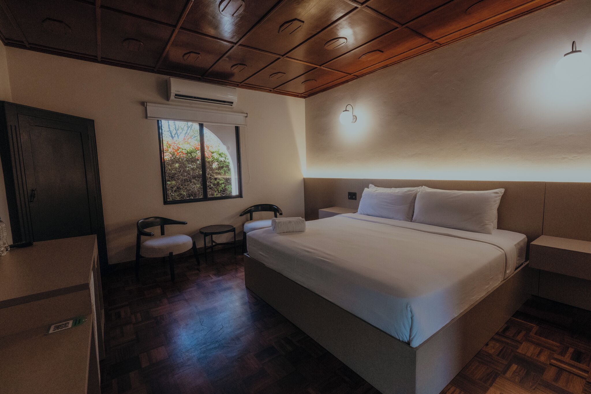Habitación de hotel con una cama grande, un escritorio, una silla y una ventana con vistas a árboles.