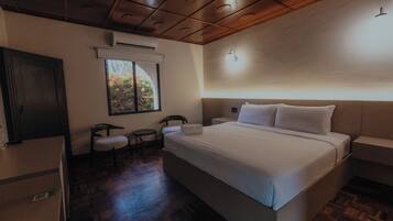 Habitación de hotel con una cama grande, un escritorio, una silla y una ventana con vistas a árboles.