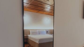 A bedroom with a large mirror, wooden flooring, a bed, and a nightstand.