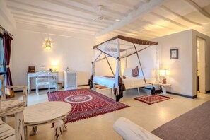Ein Schlafzimmer mit einem Himmelbett, einer weißen Kommode, einem runden Tisch und einem roten Teppich mit Muster.