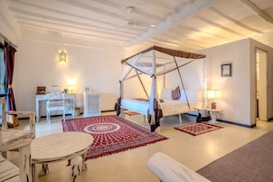 Un dormitorio con una cama con dosel, un aparador blanco, una mesa redonda y una alfombra roja estampada.