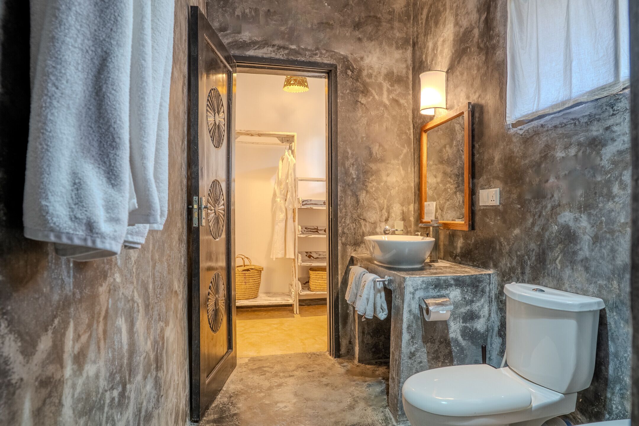 Un bagno con WC, lavandino e specchio. C'è un portascopevoli con asciugamani e un cesto. Le pareti hanno una finitura strutturata.