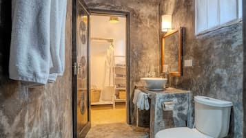 A bathroom with a toilet, sink, and mirror. There is a towel rack with towels and a basket. The walls have a textured finish.