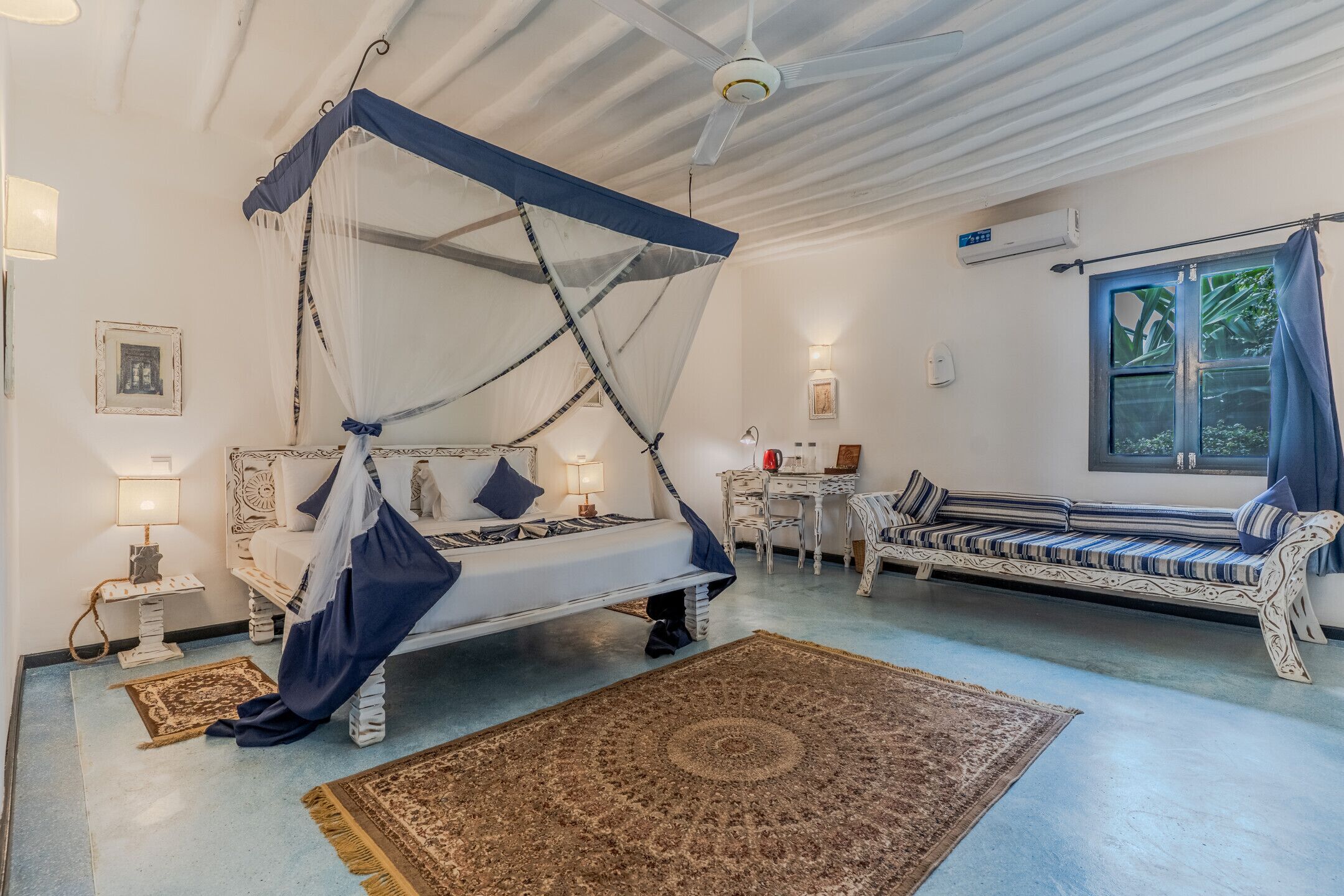 A room with a four-poster bed, a sofa, a small table, and a window with curtains.