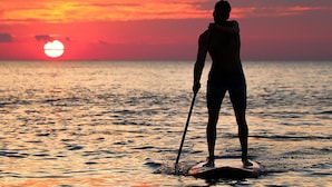 A person paddleboarding at sunset with the sun visible in the background. - Pongwe Bay Resort (Pongwe)