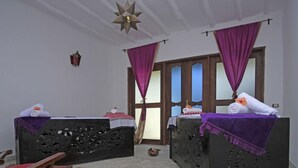 A room with two beds, each with a purple blanket and a small table beside them. There is a wooden chair and a small rug on the floor. - Pongwe Bay Resort (Pongwe)