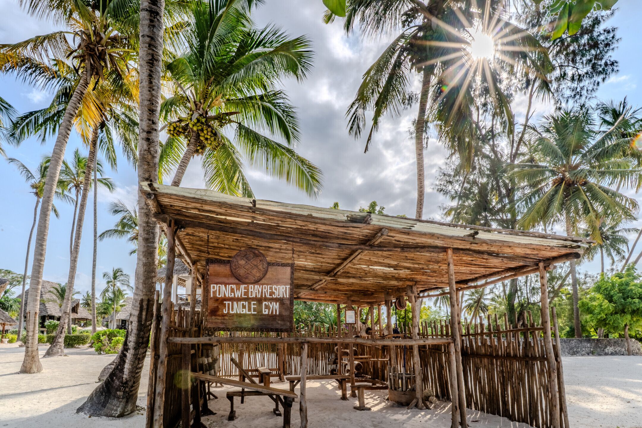 A wooden structure labeled 'Pongwe Bay Resort Jungle Gym' with a sandy ground and palm trees in the background.